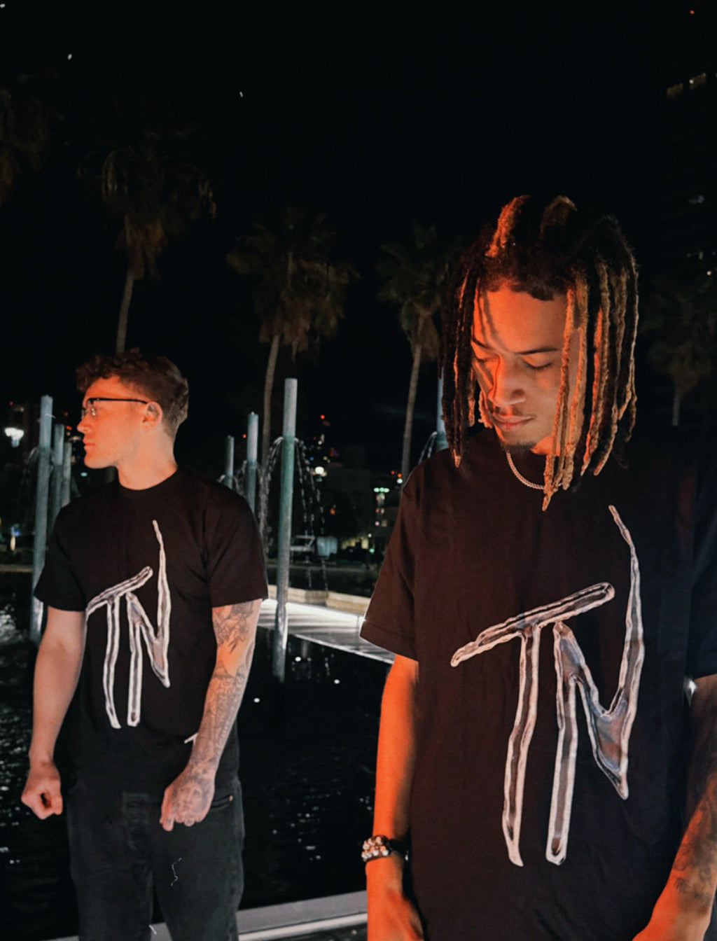 Two individuals wearing black t-shirts with a logo at night.